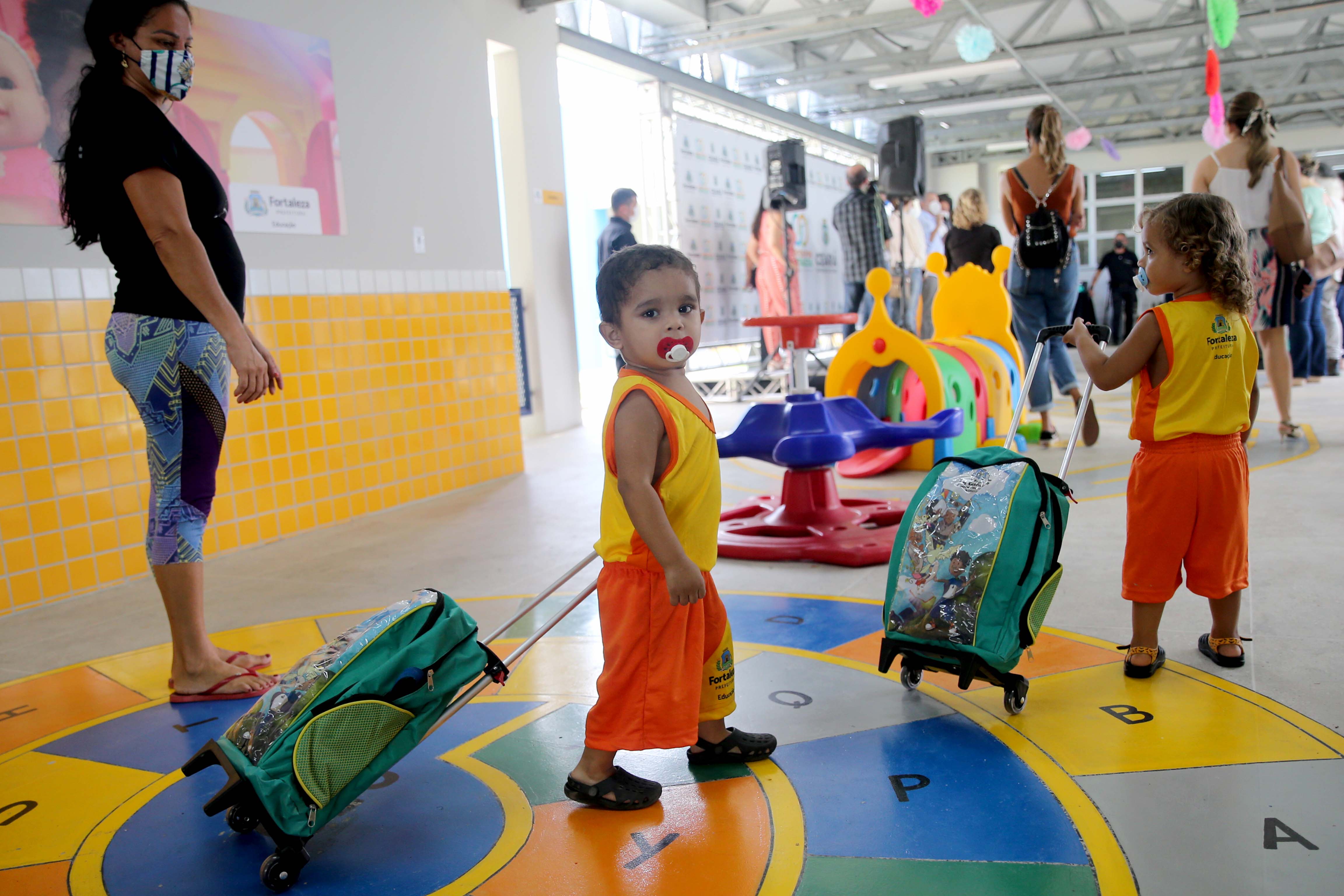 a foto mostra uma criança andando com sua mochila de rodinhas num corredor da creche